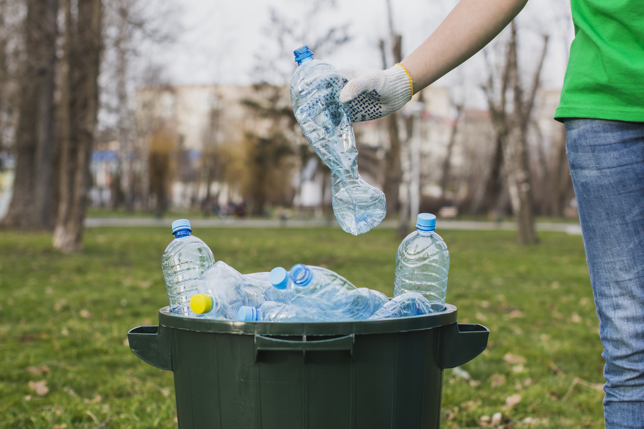 A person placing plastic bottles into a recycling bin