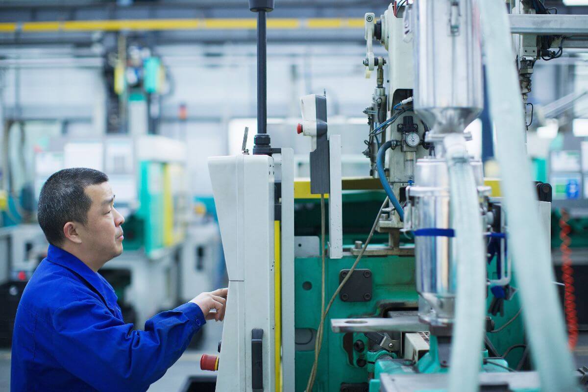 Factory technician operating industrial plastic molding equipment inside a manufacturing facility.