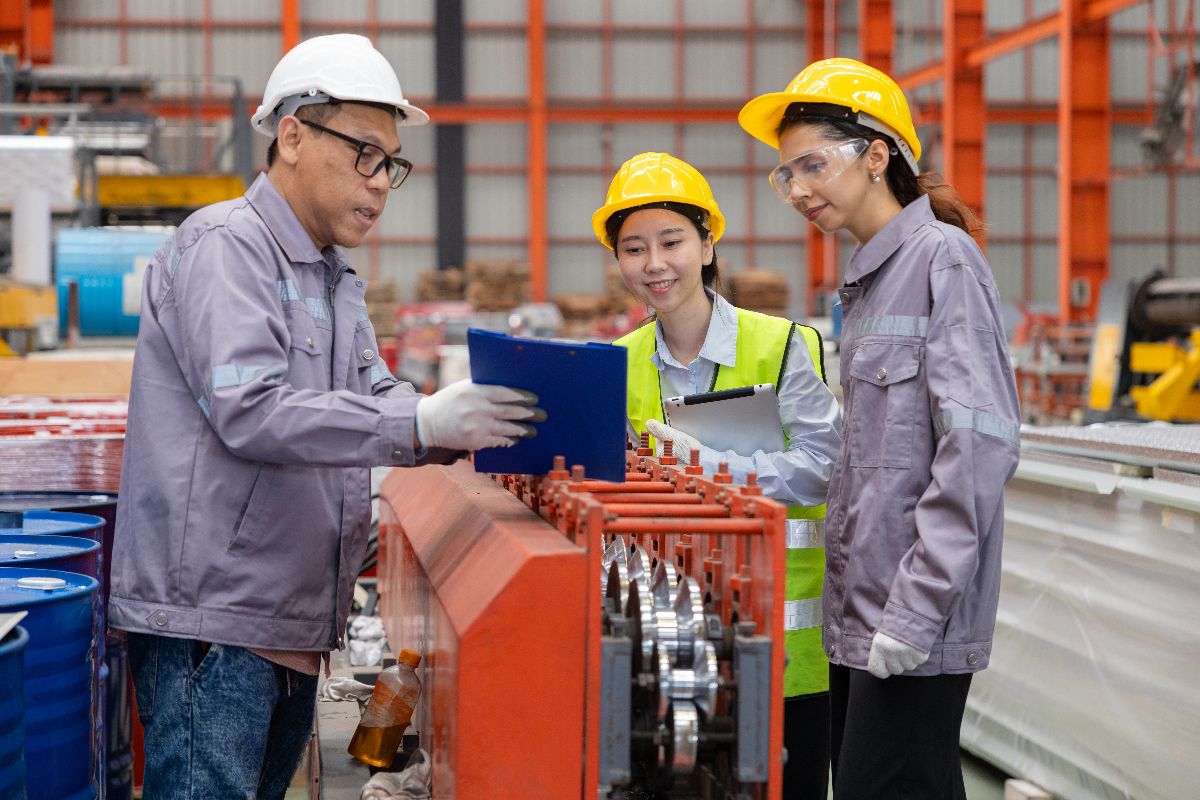 Factory engineers and technicians reviewing production processes beside industrial manufacturing equipment in a factory.