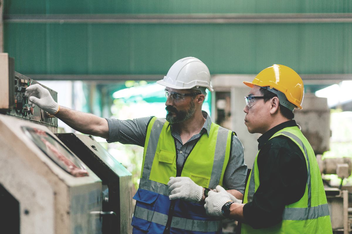 Industrial workers wearing safety gear operating and monitoring machinery in a manufacturing plant.