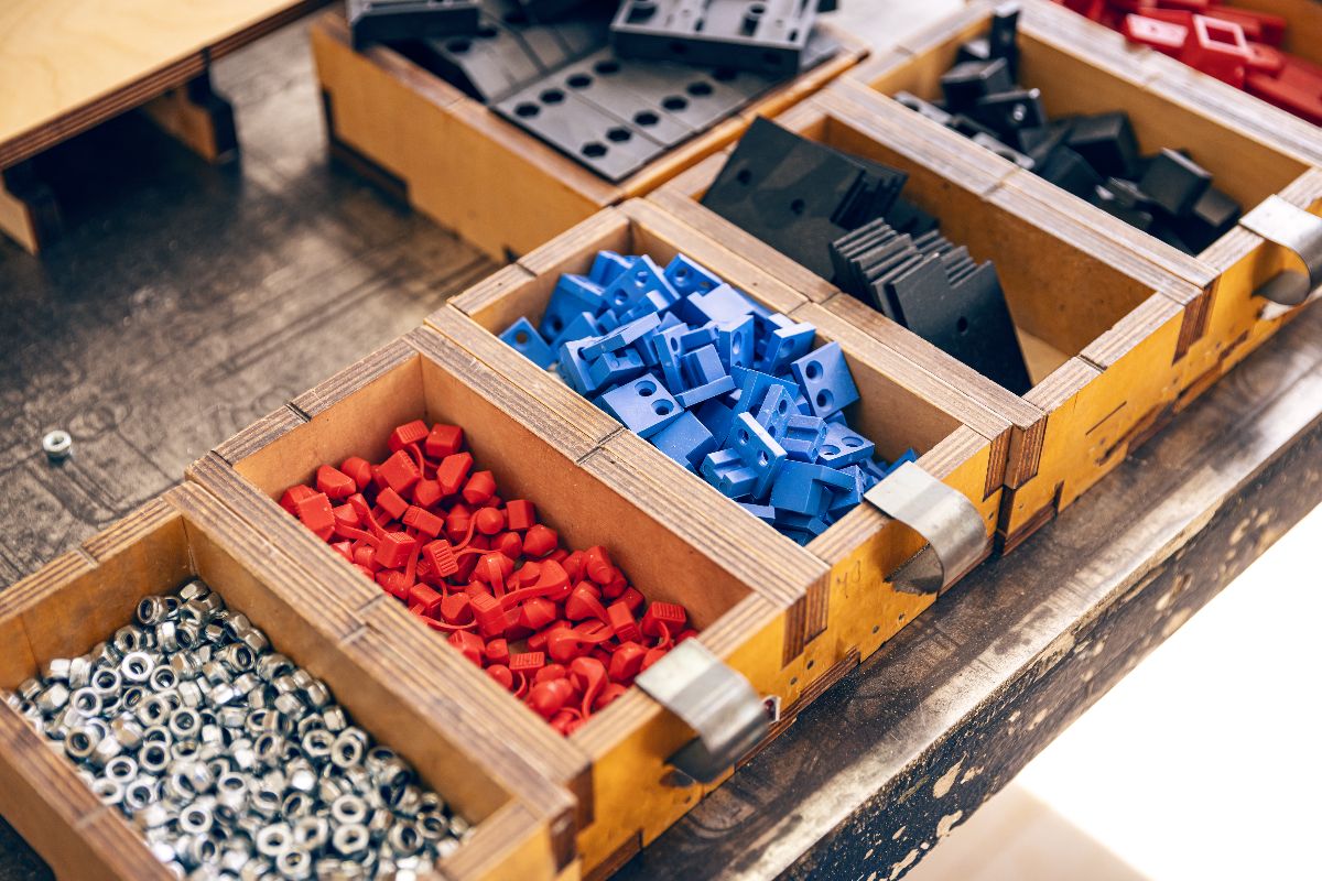 Organized trays containing colorful injection molded plastic parts and metal fasteners in a manufacturing workshop.