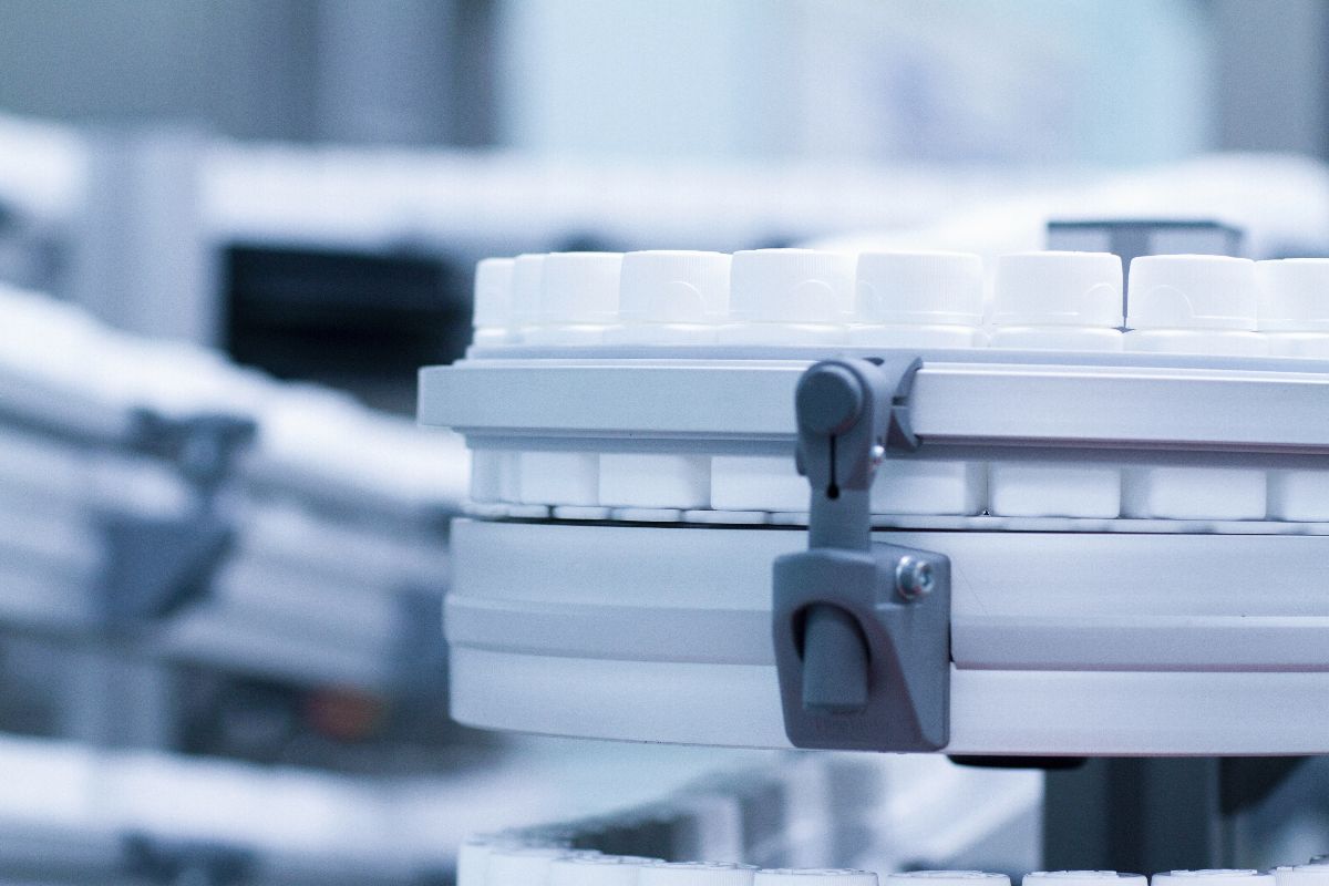 Automated manufacturing equipment handling rows of white plastic bottle caps in a production facility.